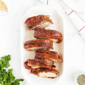 bacon wrapped pork tenderloin sliced on a long white platter