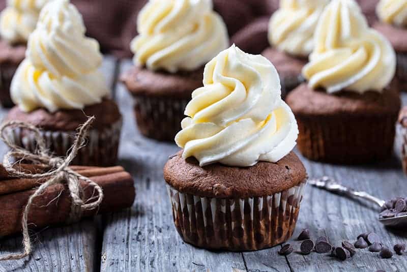 tied cinnamon sticks and chocolate chips beside chocolate cupcakes with buttercream frosting 