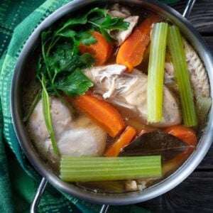 a green table cloth and boiling pan with Chicken broth made with vegetables and chicken breast , white soup bowl in a plate filled with chicken broth, salt and pepper shakers beside it