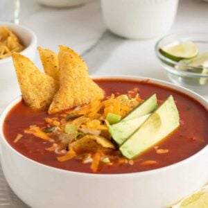 Chicken tortilla soup in a white bowl with tortilla chips and avocado slices