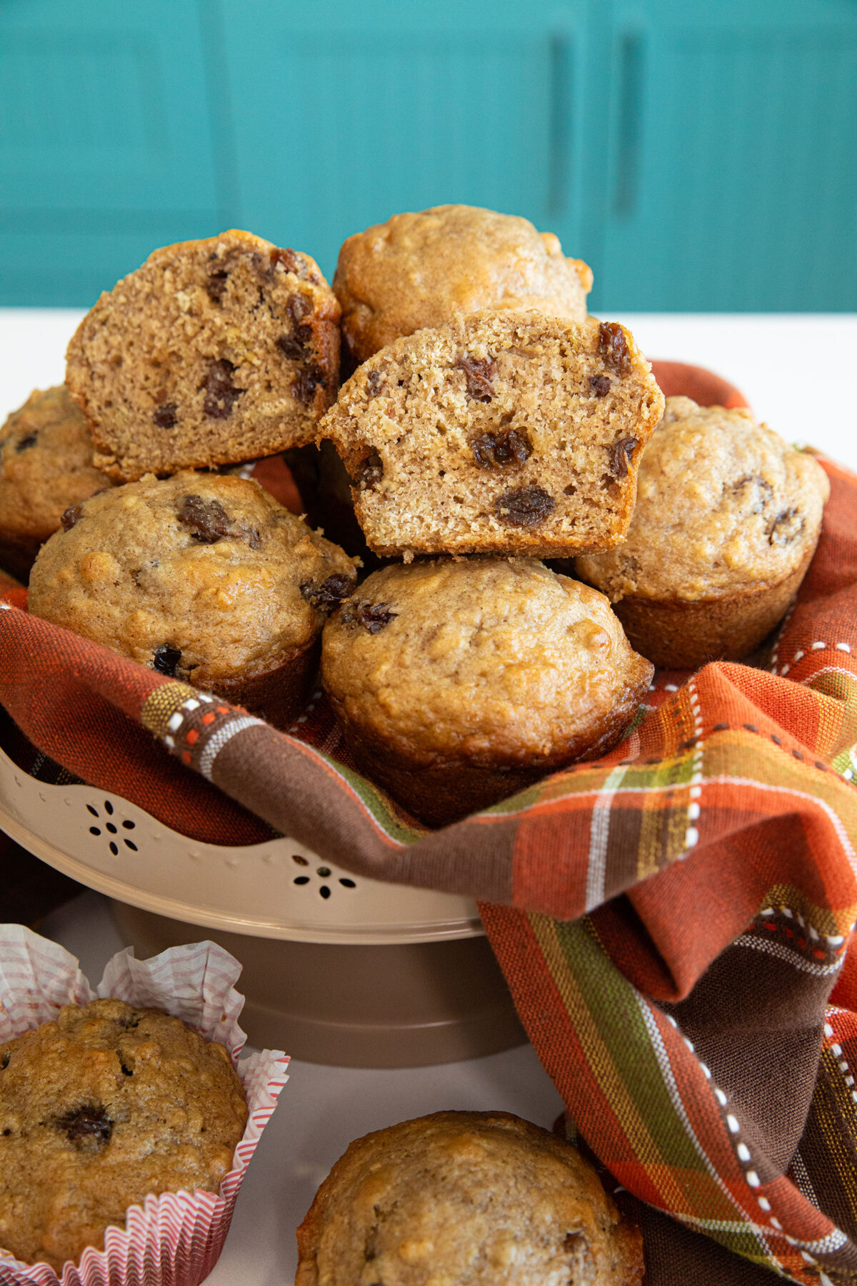 cinnamon raisin oat bran muffins on a tall bowl on a orange plaid cloth