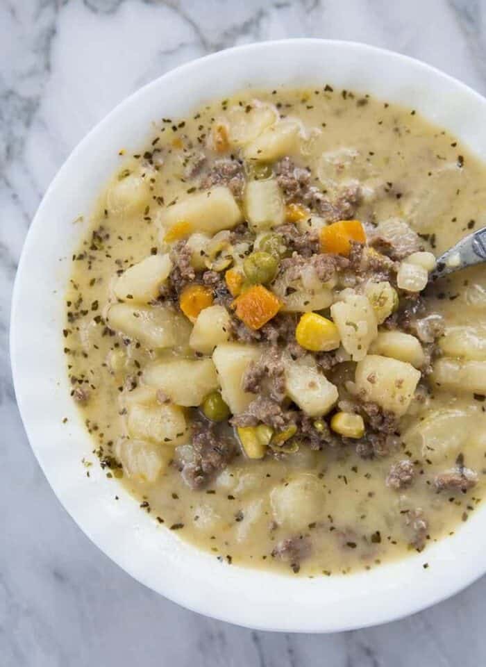 creamy potato and hamburger soup in a white soup bowl with a spoon on marble background