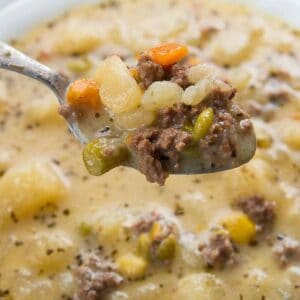 close up of a spoon full of creamy potato and hamburger soup in a white soup bowl