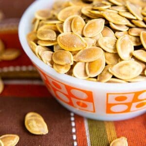 close up red orange kitchen cloth underneath a white bowl of Salty Crispy Roasted Pumpkin Seeds