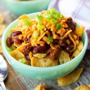 close up mint green bowl with Fritos corn chips, a spoon and kitchen towel beside it