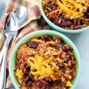 Ground Turkey Chili in small bowls with grated cheese on top, kitchen towel underneath 2 spoons