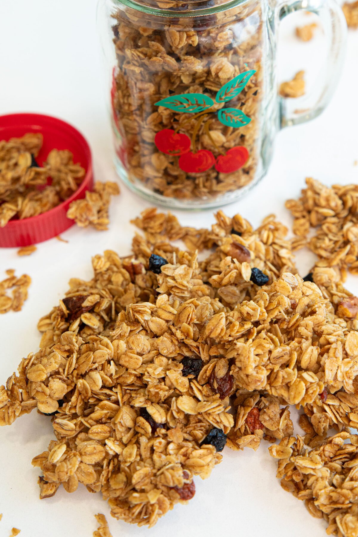 Granola clusters with dried berries on the counter with a mason jar in the background full of granola. 