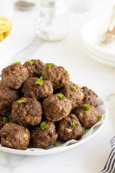 homemade meatballs piled high on a large white plate garnished with parlsey