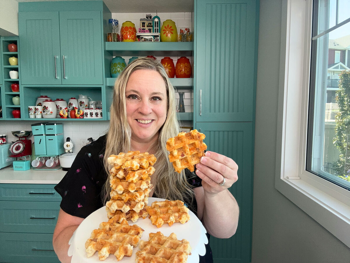 Karlynn holding up a plate full of Bacon & Cheddar Waffle Biscuits standing in her kitchen