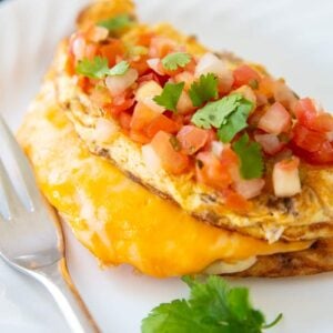 Taco Omelette top with pico de gallo and cilantro on a white plate with fork