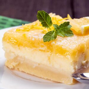 close up white plate with Lemon Cheesecake Bar garnish with lemon balm leaves