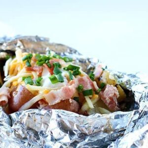 close up Campfire Grilled Loaded Baked Potatoes in a tinfoil topped with onion, cheese, sour cream, salt and pepper