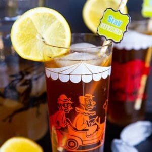 close up glass of Long Island Iced Tea garnish with slice of lemon, a pitcher and another glass on its background