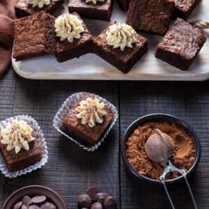 Mint Brownies with Buttercream Icing on wooden cutting board with brown tablecloth underneath and its ingredients on side