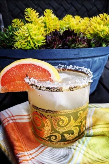 checkered tablecloth underneath a glass of Paloma Cocktail with Salted Rim garnish with a slice of grapefruit