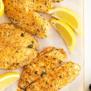 Parmesan crusted tilapia on a baking pan with slices of lemons