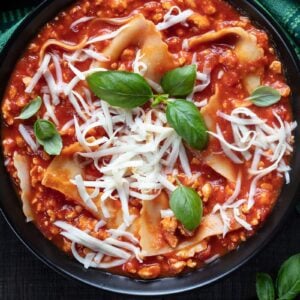 close up large soup bowl with Turkey Lasagna Soup topped with mozzarella cheese, green tablecloth underneath