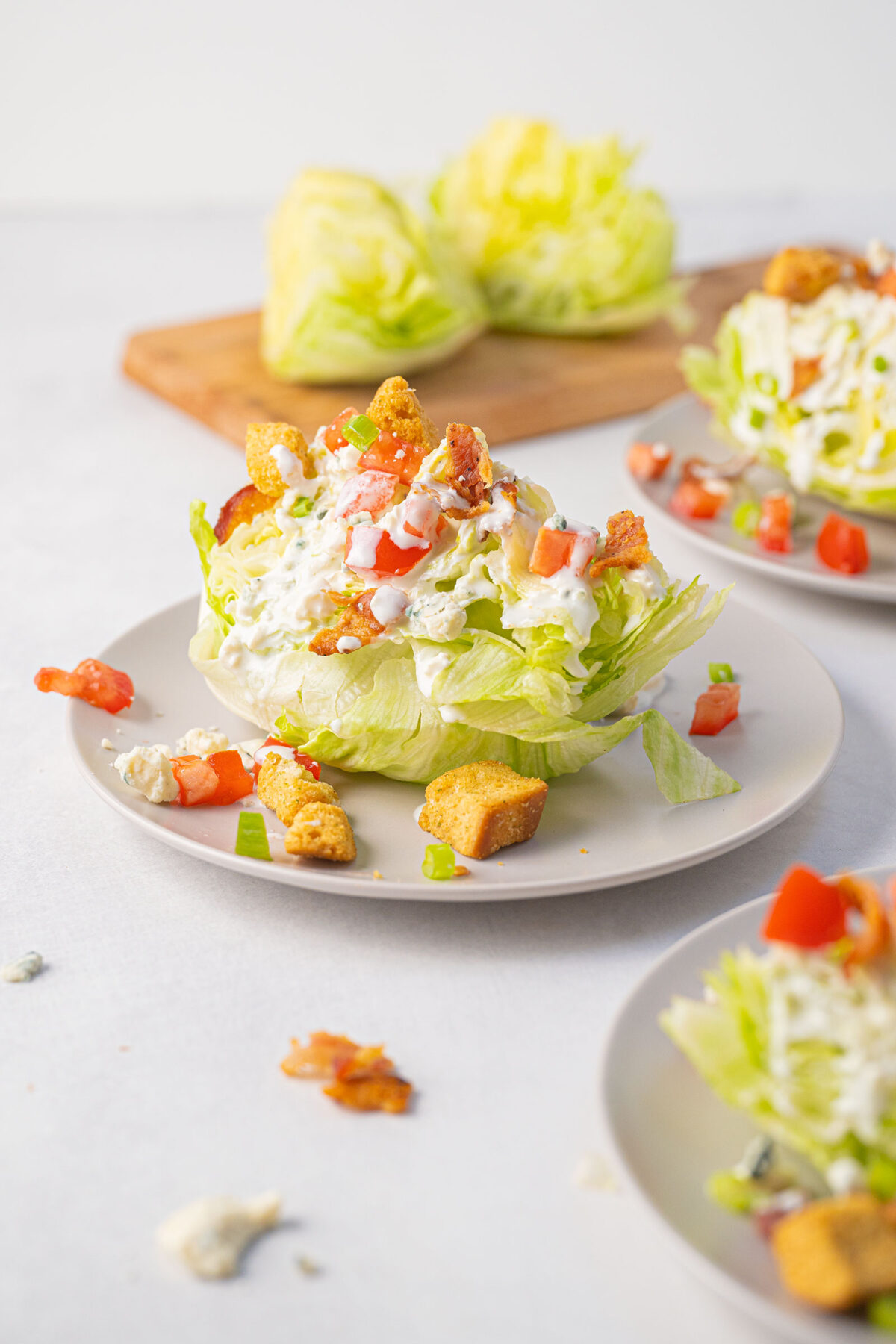 Lettuce wedge on a plate topped with dressing and tomato, bacon and croutons