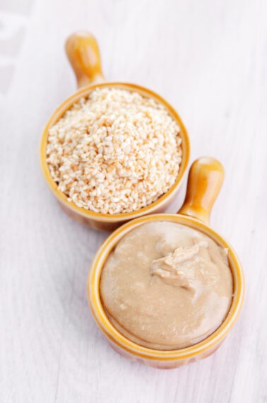 two brown bowls one with sesame seeds and one with tahini